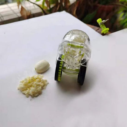 Presse-ail compact avec roues, posé à côté d’une gousse d’ail et d’ail haché – gadget de cuisine idéal pour hacher l’ail sans effort.

