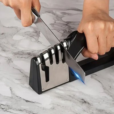 Personne utilisant un aiguiseur de couteaux professionnel sur un comptoir en marbre dans une cuisine moderne.