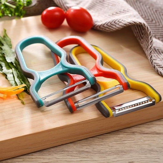 Éplucheur à légumes multifonctionnel 3 pièces en inox avec poignées colorées posées sur une planche de cuisine.