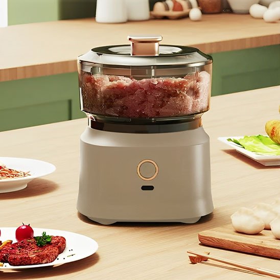 Hachoir à viande électrique moderne utilisé pour hacher de la viande crue sur un plan de travail de cuisine, entouré de plats préparés, légumes et accessoires culinaires.