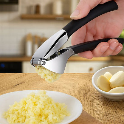 Main utilisant un presse-ail en métal pour écraser de l’ail sur une assiette blanche dans une cuisine moderne.