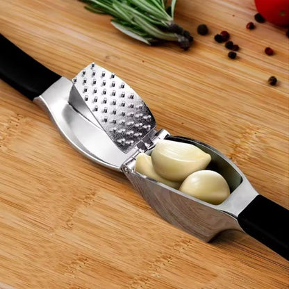 Presse-ail en acier inoxydable sur planche en bois avec gousses d’ail, romarin, poivre et tomate pour la cuisine.