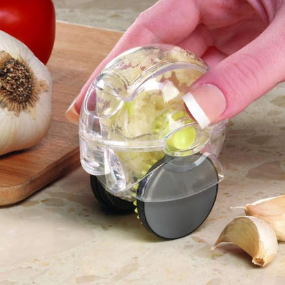 Main utilisant un presse-ail roulant transparent sur une planche en bois avec gousses d’ail - gadget de cuisine efficace pour hacher l’ail facilement.

