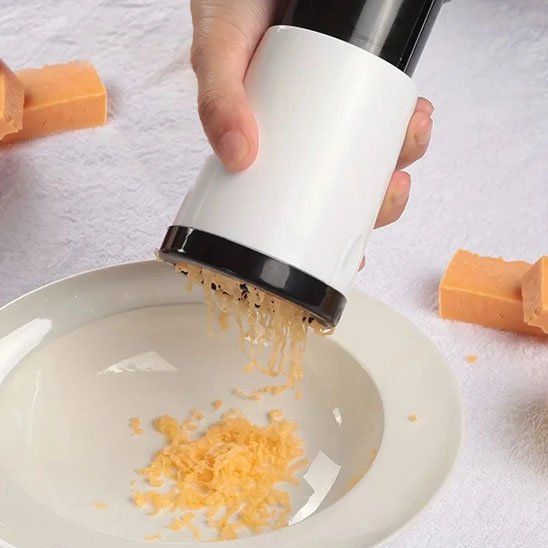 Râpe à fromage manuelle avec poignée antidérapante, utilisée pour râper du fromage frais