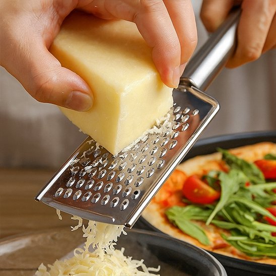 Main utilisant une râpe à fromage inox pour garnir une pizza maison – fromage râpé frais et ustensile ergonomique
