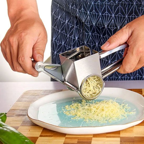Personne portant un tablier bleu utilisant une râpe à fromage rotative pour râper du fromage finement sur une assiette blanche à centre bleu
