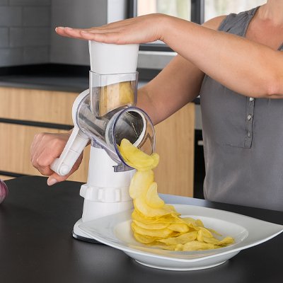 Utilisation d’une râpe à légumes manuelle pour trancher finement une pomme de terre. Les rondelles tombent directement dans une assiette, prêtes à être frites ou cuites au four.
